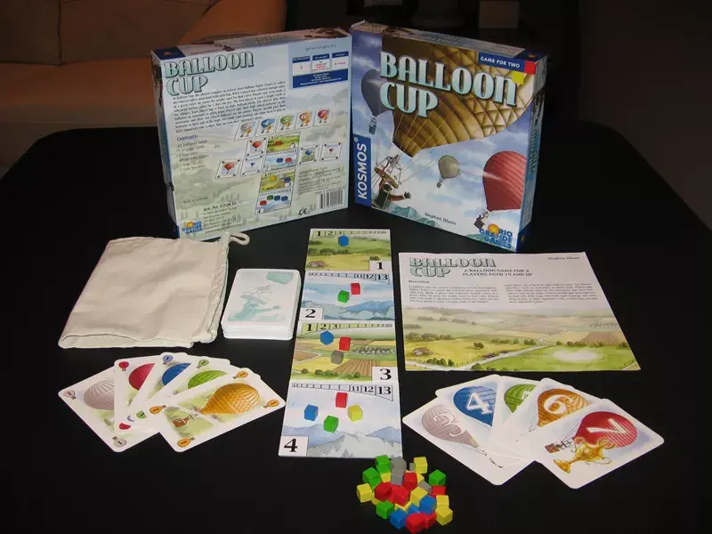 Balloon Cup card game is a fantastic 2 player game where high-valued balloons (cubes) are placed on mountains, and lower-valued balloons (cubes) are played on the plains. Players will then utilize their cards to match them with the corresponding colored cubes. Players can either put cards on their side or the opponent's side. The better balloonist takes the cubes from either the mountains or plains. When a player gets enough of the same color cubes, they are rewarded with 1 of the 5 trophies. The game is played until one of the balloonists wins 3 trophies. This game is quick and super simple to play. Through the years, this game has inflated in price from its retail price since there are not many copies out there.