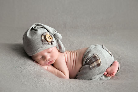 newborn baby boy on his belly dressed in a pair of gray pants with plaid pocket and matching hat