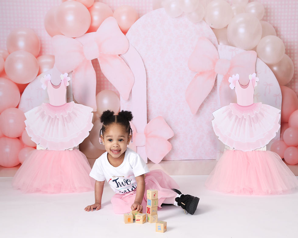 A child in a white shirt and pink tutu plays with blocks. Pink balloons and dress cutouts decorate the background. The mood is joyful.