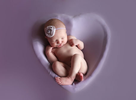 newborn baby girl in heart shaped bowl on her back on a lavender background