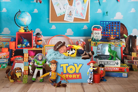 newborn baby boy dressed as woody in a toy story box with toy story character in andy's room