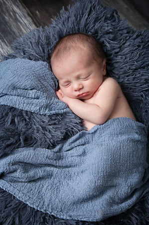newborn baby boy laying on a blue fur drapped with a blue wrap
