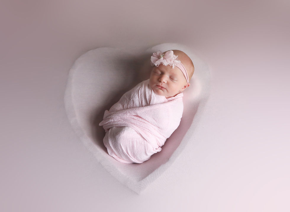 Newborn baby girl wrapped in pink in a heart bowl