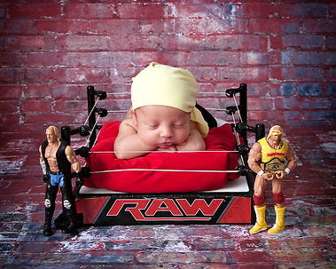 newborn baby boy in a wrestling ring with a yellow rag on his head and wrestling rubber figures