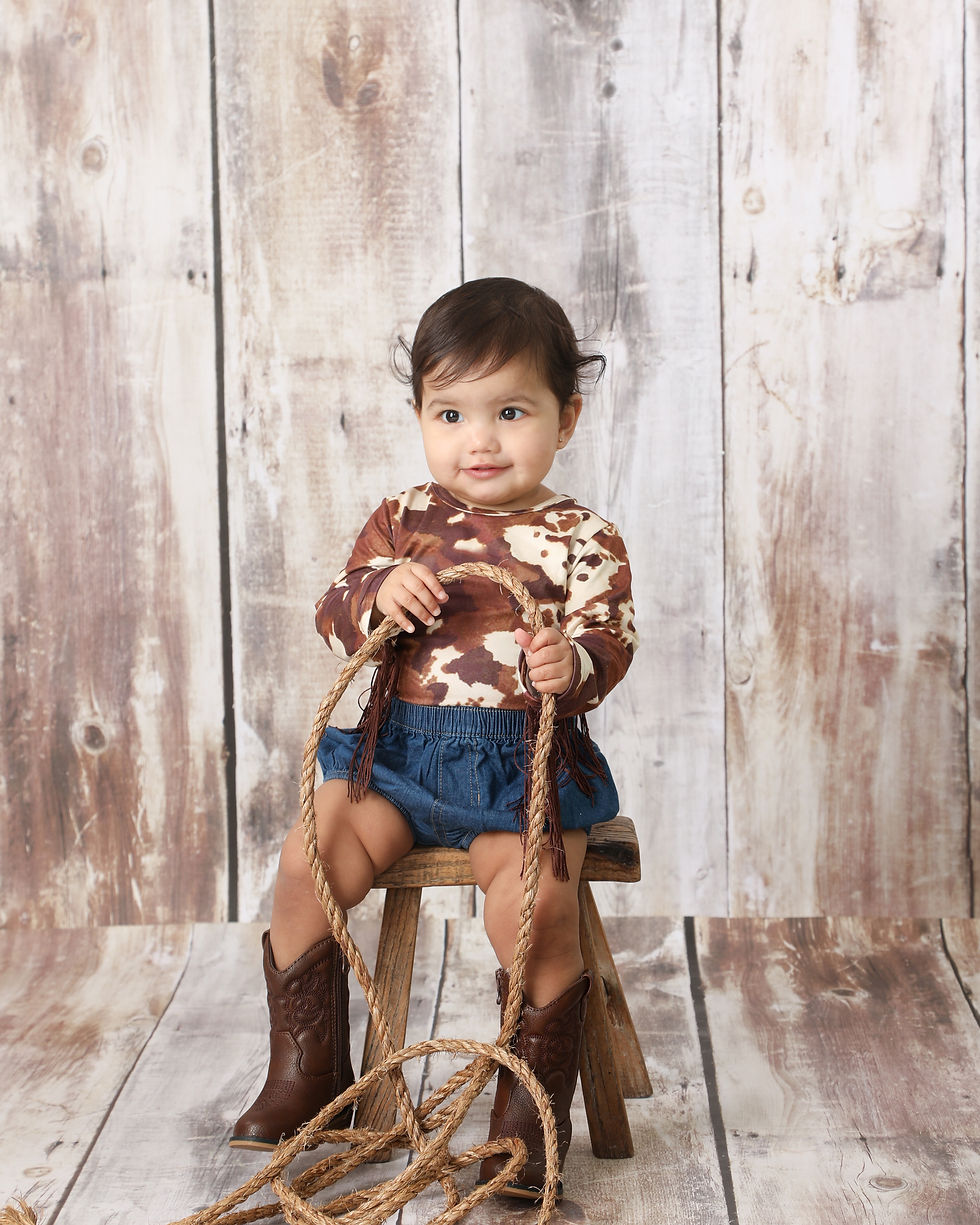 Girl sitting on a bench with a rope. She is dressed as a cow girl.