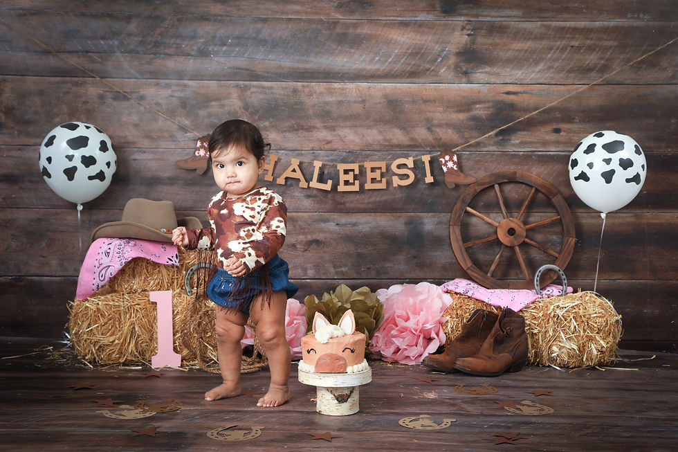 Girl standing with cow balloons, wagon wheel, boots, hay bales , horse shoe and western hat.