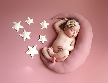 newborn baby girl on her back legs crossed on a pink moon with stars