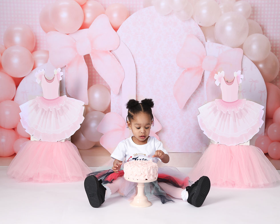 Toddler in a tutu sits on floor, touching pink cake. Background features pink balloons and ballerina dress cutouts, creating a festive mood.
