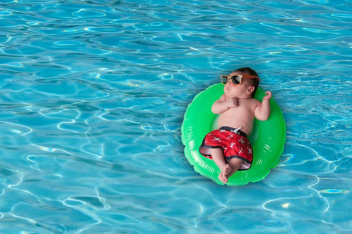 newborn baby boy floating on a pool tube wearing swim trunks and sunglasses