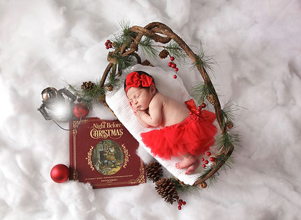 newborn baby girl laying on a twig bed in thw snow with the night before christmas book and lantern