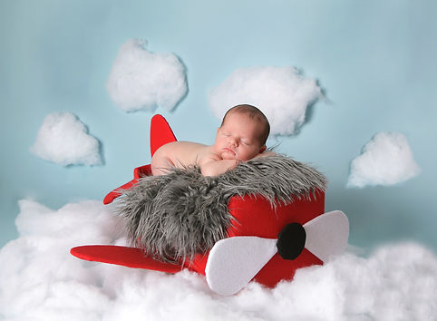 newborn baby boy in a handmade red airplane in the clouds