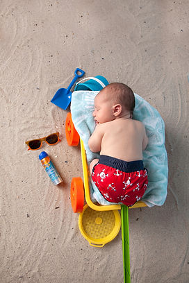 newborn baby boy in a sand wagon in the sand with sand toys , sunglasses and sunscreen
