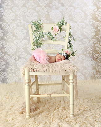 newborn baby girl laying on a cream colored chair