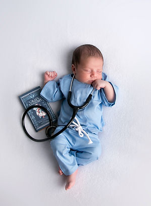 newborn baby boy dressed in a blue doctor's scrub with a stethescope and gray's anatomy book