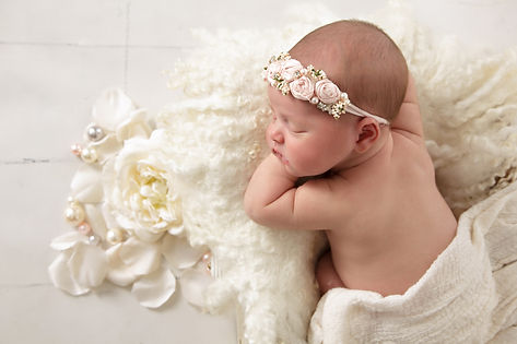newborn baby girl on her belly with cream colores flowers and beads
