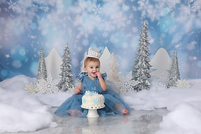 baby girl in blue dress with snow and birthday cake