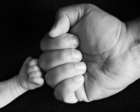 black and whit image of newborn baby's fist against his dad's fist