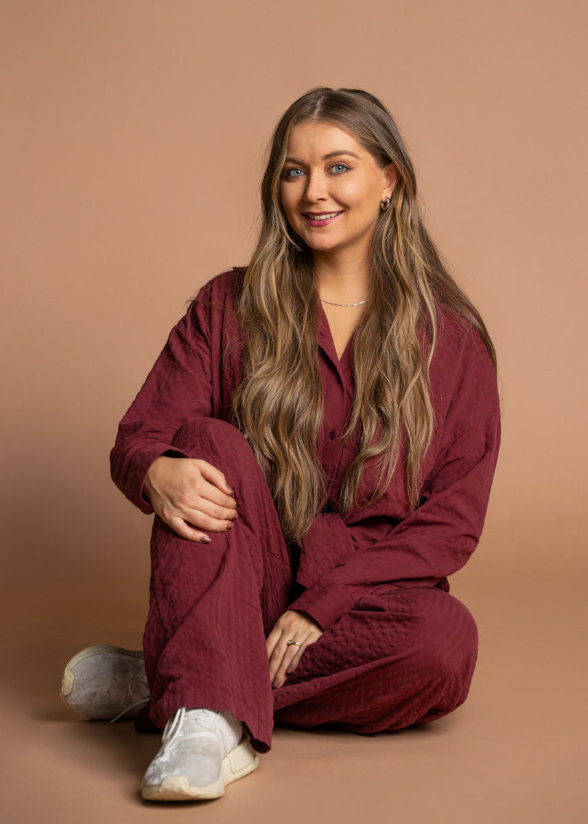 Melissa, Mamalabin toinen perustajista, kuvattuna studiossa beigellä taustalla burgundin värisessä asussa.