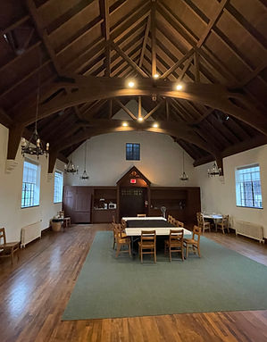 Large hall featuring exposed wooden ceiling beams, polished hardwood floors, and a small cluster of tables and chairs on a central rug.