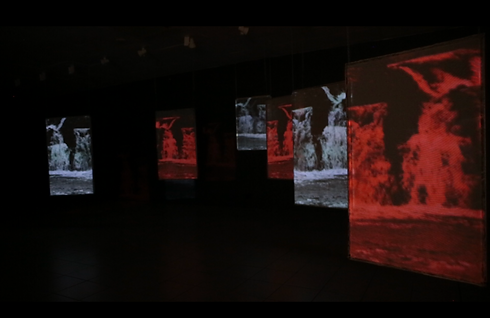 Art installation with several illuminated screens, displaying a red and white projected art.