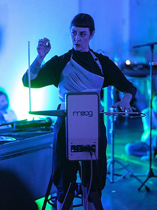 Lola de la Mata playing theremin with Moog logo during performance in a dimly lit setting