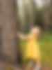 Niña en el bosque tocando el tronco de un árbol y mirando hacia el cielo.