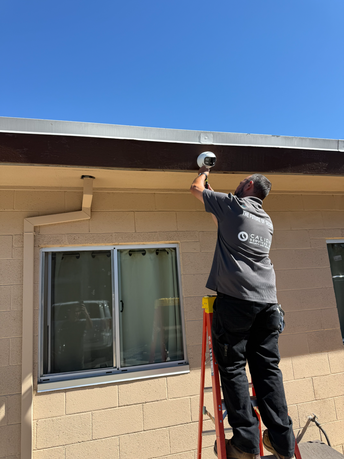 Calidad Services technician installing a security camera under a building eave