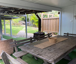 back of house covered area with large wooden outdoor table, wooden bench seating, outdoor fireplace, green grass