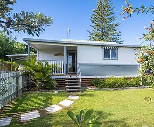 tin and fibro front of a beach house in Wooli with a front garden, green trees and shrubs with stairs to front door