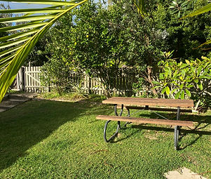 back yard with green grass, wooden picket fence, shrubs and trees and a picnic table
