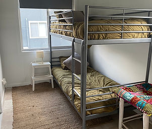 single bunk beds with green quilt covers, rush matting, sunny window, bedside table and lamp