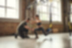 Doing squat exercise. Confident young personal trainer is showing slim athletic woman how