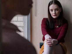 Teenage girl sitting against the wall facing another person