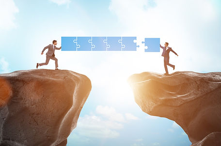 Two business people divided by a chasm but completing a puzzle piece to create a link