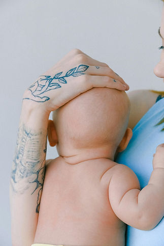 A baby being gently held, with a clear view of the back of their head, showcasing a flattened area associated with brachycephaly in babies. The image emphasizes parental care and the importance of monitoring head shape development.