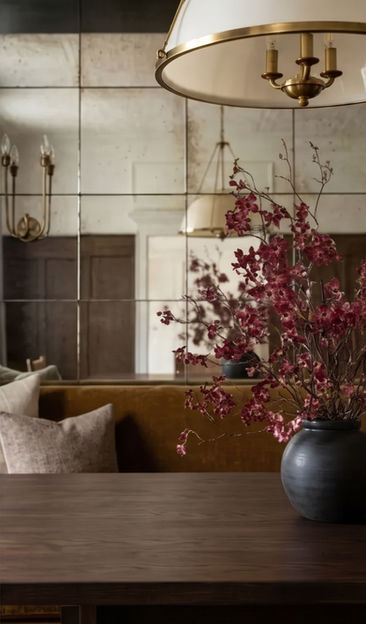 Burgundy floral branches in a black ceramic vase against antique mirror panels and dark wood wainscoting.
