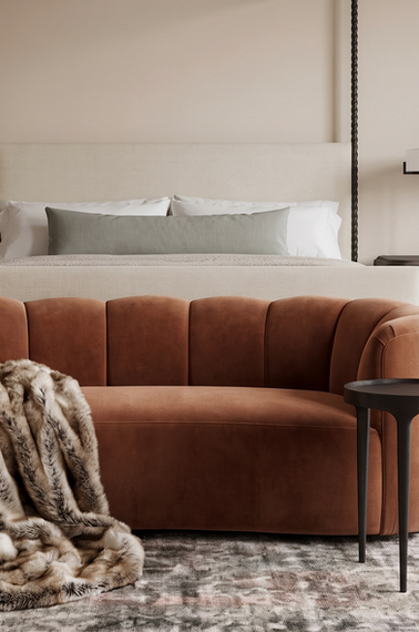 Curved rust velvet bench positioned at the foot of a gray upholstered bed in a warm Spanish Revival bedroom.