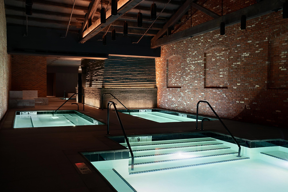 Indoor spa with warm lighting, featuring three lit pools surrounded by brick walls and modern design elements. Calm ambiance.