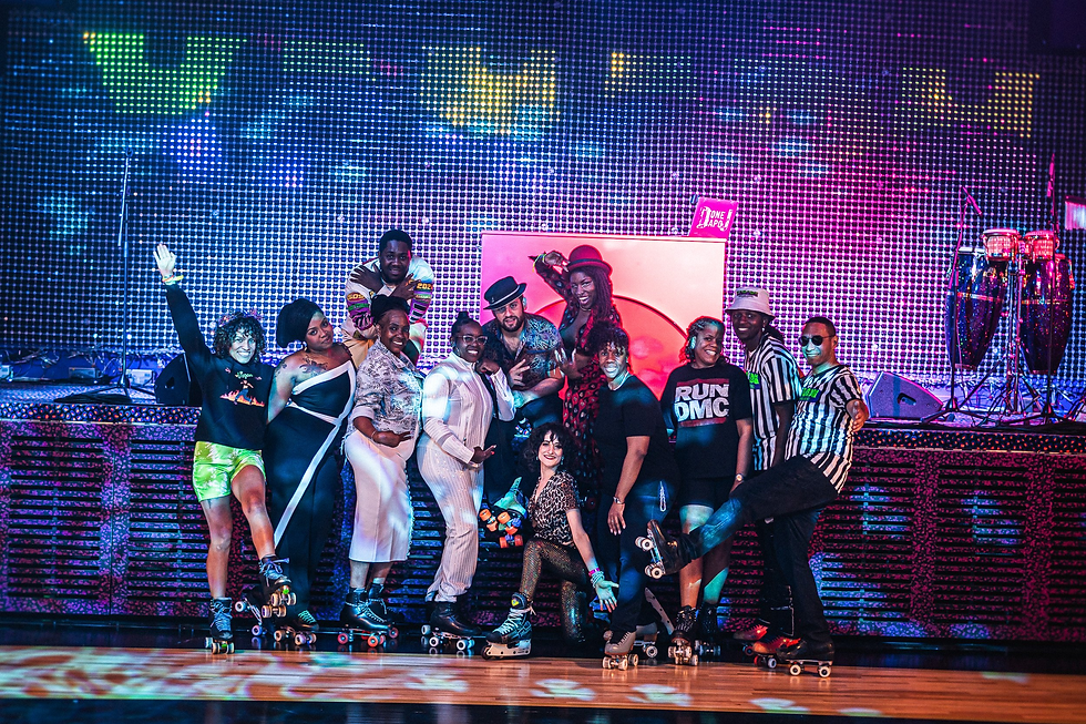 Group of smiling people wearing vibrant outfits and roller skates pose together. Colorful LED backdrop and vibrant stage lighting set a lively mood.