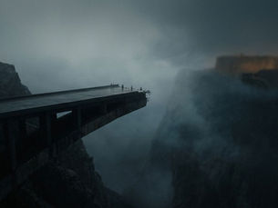 A broken bridge juts into foggy abyss; birds perch on the edge. A fortress looms distantly through the mist, creating a mysterious mood.