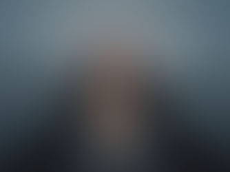 Person in a coat walking on a foggy stone bridge towards a glowing lantern. The scene is misty and atmospheric, creating a mysterious mood.
