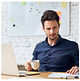 Man with cup in and laptop looking down at something 