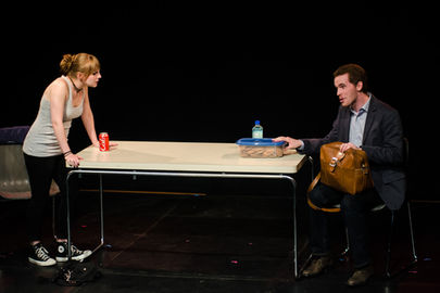 Two actors bickering on stage with a can of Coke and a tub of cookies.