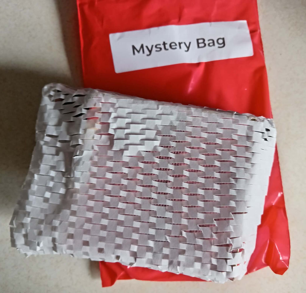 Red mystery bag labeled Mystery Bag with a silver woven package on a beige surface, suggesting a gift or surprise.