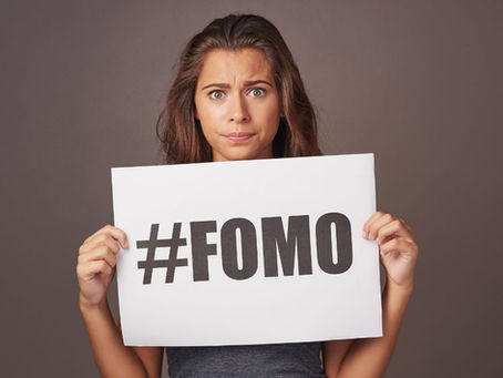 A woman holding up a hastag sign for FOMO, the fear of missing out
