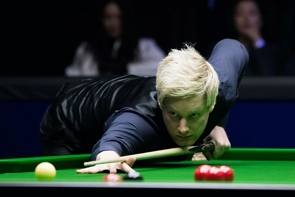 A focused person plays snooker, aiming at red balls on a green table. Spectators in the blurred background convey a tense atmosphere.