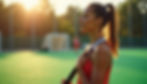 Woman in a coral tank top meditates on a field at sunset, holding a hockey stick, with a blurred goal in the background.