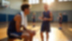 Two basketball players in blue jerseys converse on a sunlit indoor court. One sits with a towel, while others practice in the background.