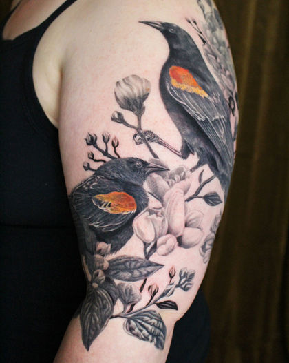a tattoo of two blackbirds and some white florals on a woman's arm