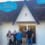 A group of six people standing at the storefront for Reloved Ineriors, smiling and celebrating a grand opening